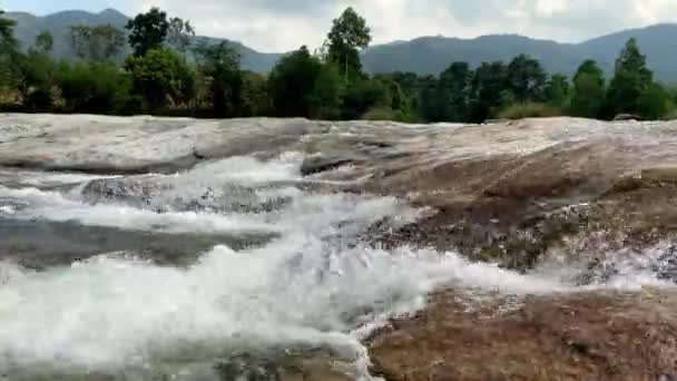 Een waterval naast een rivier. bergstroom stroomt door grote stenen, schuim uit de stroming van water — Stockvideo