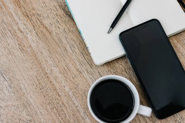 Düz kompozisyon, not defteri, akıllı telefon, bir fincan kahve ve kahvaltı kurabiyesi. O gün için bir plan kaydet. Sabah işyerinde. Açık bir kağıda yazmak için bir kalem. Boşluğu kopyala, metin için boşluk