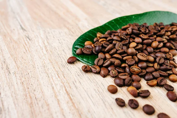 Yeşil yapraklı kahve çekirdekleri ve açık ahşap bir masaya yayılmış taze americano, espresso, doğal arka plan, üst manzara, yakın çekim tanecikleri, düz yatak, metin eklemek için yer, kopyalamak için yer