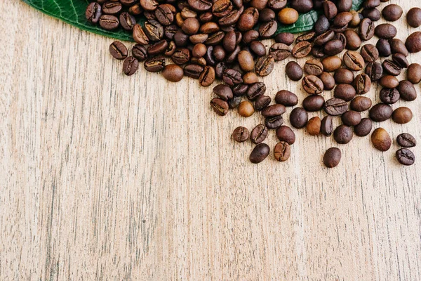 Yeşil yapraklı kahve çekirdekleri ve açık ahşap bir masaya yayılmış taze americano, espresso, doğal arka plan, üst manzara, yakın çekim tanecikleri, düz yatak, metin eklemek için yer, kopyalamak için yer