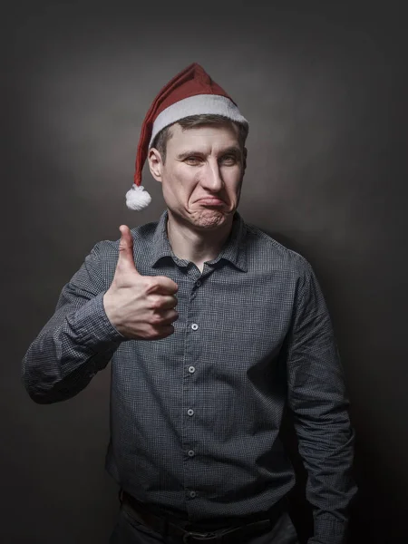 Young handsome man dressed in a Santa Claus hat on a gray backgr — Stock Photo, Image