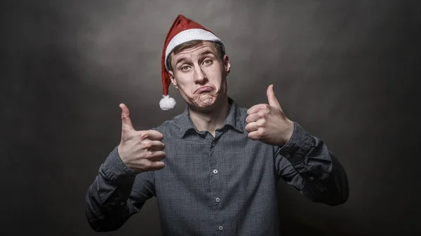 Young handsome man dressed in a Santa Claus hat on a gray backgr — Stock Photo, Image