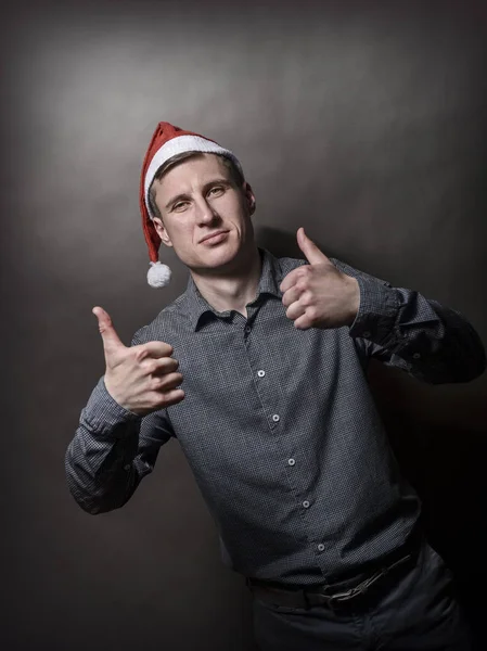 Young handsome man dressed in a Santa Claus hat on a gray backgr — Stock Photo, Image