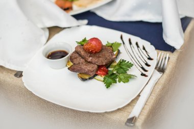 Güzel iştah açıcı yemekler, rosto, et ürünü et, sos, domates ve otlar beyaz bir tabakta, mutfakta ve servis ediliyor..