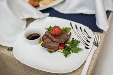 Güzel iştah açıcı yemekler, rosto, et ürünü et, sos, domates ve otlar beyaz bir tabakta, mutfakta ve servis ediliyor..