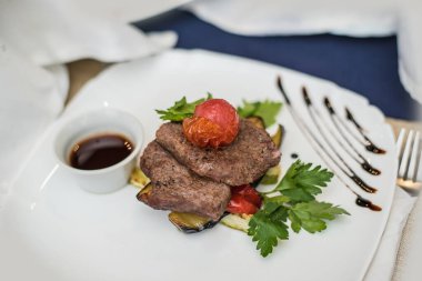 Güzel iştah açıcı yemekler, rosto, et ürünü et, sos, domates ve otlar beyaz bir tabakta, mutfakta ve servis ediliyor..