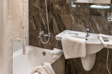 Moda ve pahalı bir banyo ve tuvaletin içi kahverengi dekoratif taş ve fayanslardan yapılmıştır, beyaz seramik ve solgunluk elementleriyle..