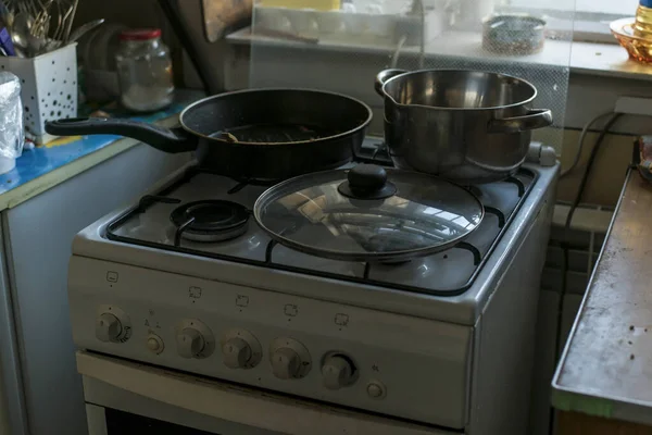 Gas stove and pans and pans on it in the interior of a small cheap kitchen with cutlery and kitchen appliances.