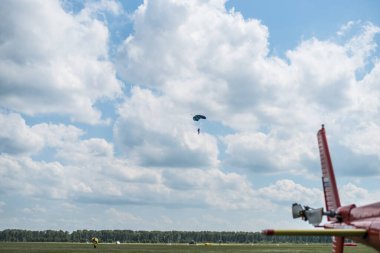 Mavi bir yaz gökyüzünde beyaz bulutların arka planında iniş yapan bir paraşütçü ile hava sahasının güzel manzarası..