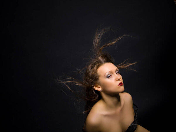 Conceptual portrait of a fashionable young, seductive, emotional, beautiful girl, woman, with her hair loose and developing in the wind, on a dark background.