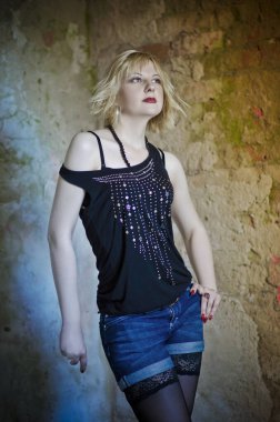 Modern ve genç, baştan çıkarıcı, duygusal, güzel bir sarışının kavramsal portresi. Koyu bir bluz, yırtık tayt ve çorap giymiş bir kadın. Yıkık bir binanın, duvarların, tuğlaların içinde.