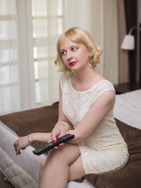 Genç, baştan çıkarıcı, güzel bir sarışının, beyaz elbiseli bir kadının kavramsal portresi. Tüketici elektroniğinden uzaktan kumandalı bir yatakta oturuyor. Bir otel odasının içinde, dairelerde.