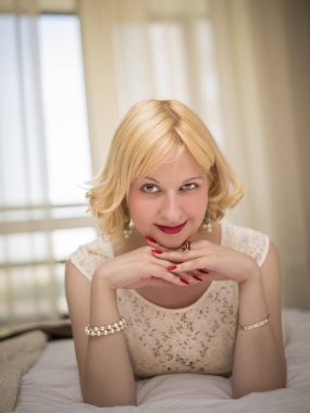 Genç, baştan çıkarıcı, duygusal, güzel bir sarışının, beyaz elbiseli bir kadının, otel odasının içinde, yatağında uzanan bir kadının kavramsal portresi.