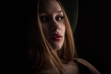 Modaya uygun genç, baştan çıkarıcı, duygusal, güzel bir kız, sarı düz saçlı, dudaklarında kırmızı ruj, siyah bir elbise ve siyah bir arka planda şapkası olan bir kadın..