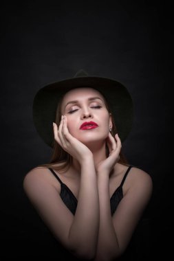 Modaya uygun genç, baştan çıkarıcı, duygusal, güzel bir kız, sarı düz saçlı, dudaklarında kırmızı ruj, siyah bir elbise ve siyah bir arka planda şapkası olan bir kadın..