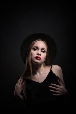 Modaya uygun genç, baştan çıkarıcı, duygusal, güzel bir kız, sarı düz saçlı, dudaklarında kırmızı ruj, siyah bir elbise ve siyah bir arka planda şapkası olan bir kadın..
