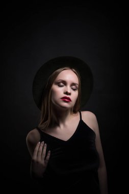 Modaya uygun genç, baştan çıkarıcı, duygusal, güzel bir kız, sarı düz saçlı, dudaklarında kırmızı ruj, siyah bir elbise ve siyah bir arka planda şapkası olan bir kadın..