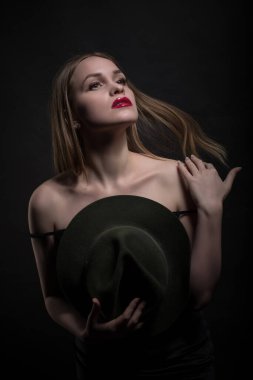 Modaya uygun genç, baştan çıkarıcı, duygusal, güzel bir kız, sarı düz saçlı, dudaklarında kırmızı ruj, siyah bir elbise ve siyah bir arka planda şapkası olan bir kadın..