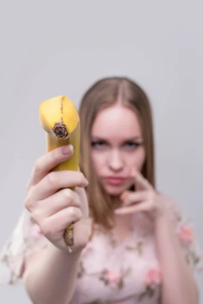 Konzeptporträt eines modischen jungen, verführerischen, emotionalen, schönen Mädchens und einer Frau mit blonden glatten Haaren, mit einer Banane in den Händen, auf hellgrauem Hintergrund. — Stockbild Konzeptporträt Eines Modischen Jungen Verführerischen Emotionalen Schönen Mädchens Und Einer — Stockfoto