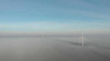 Güneşin doğuşunda sisli bir sabahta dönen tek bir yel değirmeni. Rüzgâr enerjisi çiftliğinin arkasındaki inşaat alanı. Yeşil, temiz, yenilenebilir enerji. Hava görüntüleri.
