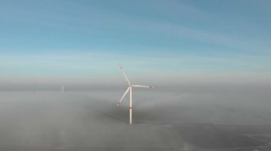 Güneşin doğuşunda sisli bir sabahta dönen tek bir yel değirmeni. Rüzgâr enerjisi çiftliğinin arkasındaki inşaat alanı. Yeşil, temiz, yenilenebilir enerji. Hava görüntüleri.