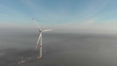 Rüzgar enerjisi çiftliğinin inşaat alanı. Güneşin doğuşunda sisli bir sabahta dönen iki yel değirmeni. Yeşil, temiz, yenilenebilir enerji. Hava görüntüleri.