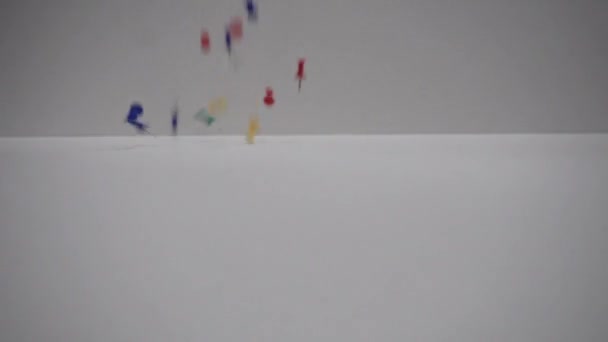 Botones multicolores para el tablero. Pasadores cayendo sobre una mesa blanca. 250FPS de cámara lenta — Vídeos de Stock