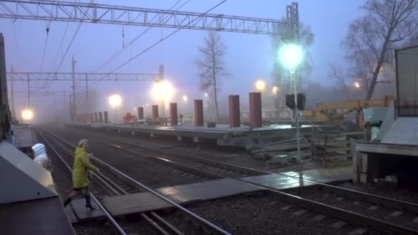 Russland, dolgiprusniy - 08. November 2019: früher Morgen. Nebel. Ein Radfahrer und eine Frau überqueren die Bahngleise vor dem fahrenden Zug. Das Video flackert. Leitartikel — Stockvideo