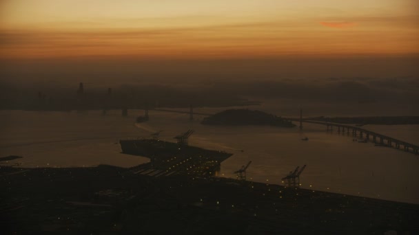 照らされたオークランド港やドック湾橋私たち 高速道路宝島 サンフランシスコ市高層ビル カリフォルニア アメリカの空中日没ヘイズ ビュー — ストック動画