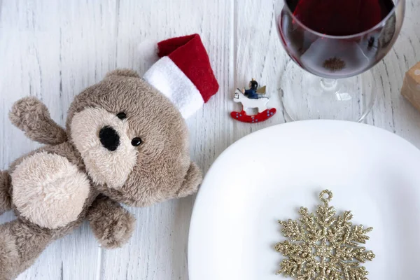 New Year\'s table setting. Toy bear in Santa\'s hat, snowflake, plate and glass with red wine. Happy New Year and Merry Christmas