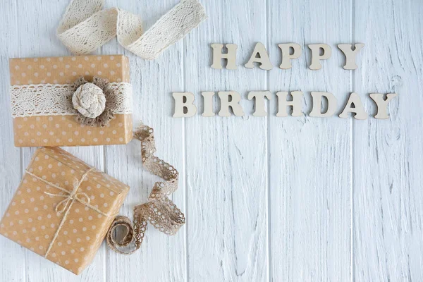 Happy Birthday. Greeting inscription from wooden letters on a light wooden background with a gift. Greeting card with a gift and the inscription. View from above