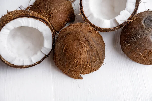 Close-up de um fruto de coco quebrado em um fundo de madeira branco com um lugar para inscrição. Banner para centro de spa, dieta saudável, óleo de coco para alimentos e corpo . — Fotografia de Stock