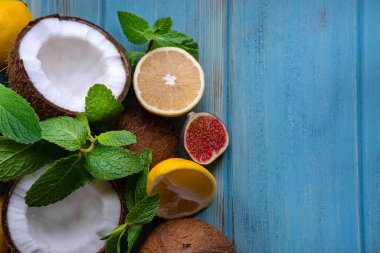 Mavi ahşap zemin üzerinde limon ve nane yapraklarıyla doğranmış hindistan cevizi yarıları. Hindistan cevizi sitrusu ve fotokopi alanı olan tropikal egzotik bir arka plan. Yukarıdan görüntüle