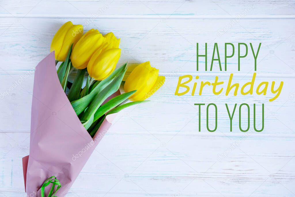 Birthday greeting card with yellow tulips and the inscription on a light wooden background. Greeting card for posting, blog posting for a birthday. View from above