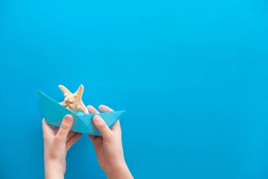 Deniz temalı bir pankart tasarla. Denizyıldızı ve kağıttan bir tekne mavi üniformalı bir çocuğun ellerinde. Seyahat, turizm, deniz, açık hava aktiviteleriyle ilgili metin çerçevesi