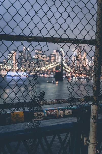 View through metal mesh on Brooklyn Bridge and Manhattan Bridge night skyline panorama in Manhattan, New York, USA