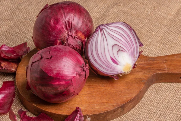 Drei frische rote Zwiebeln, eine geschnitten, auf einem Tisch — Stockfoto