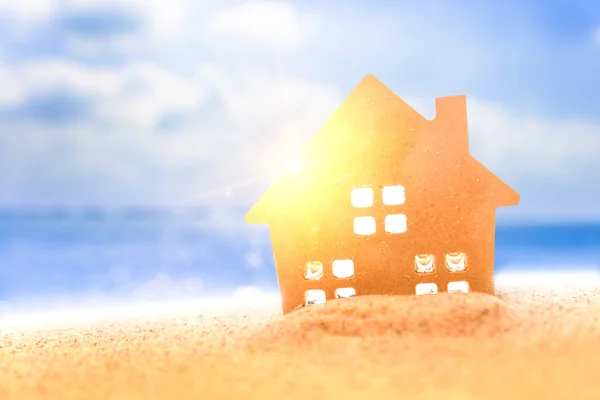 Closed up tiny home models on sand with sunlight and beach background.