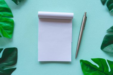 Çerçeve olarak tropikal yaprak ile boş alan beyaz defter ve kalem üst görünümü.