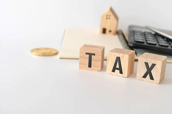 Tax word on wooden cube with objects as gold coin, calculator and mini home model behide white clean background. Business financial loan property concept.Tax word on wooden cube with objects as gold c — ストック写真