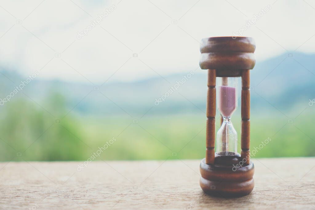 Small vintage hourglass show time is flowing never return with nature background.