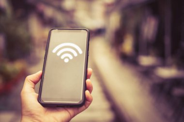 Açık alan arka planında wifi ikonu olan akıllı telefon kullanan bir kadın. İş iletişimi sosyal ağ kavramı.