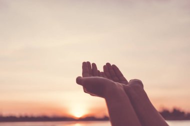 Kadın elleri, doğanın önünde dua eder gibi bir araya gelir plajda gün batımının arka planında.