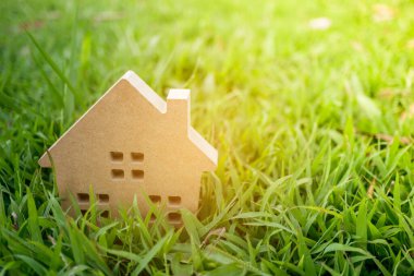 Güneş ışığı arka plan ile yeşil çim üzerinde küçük ev modeli kapalı.