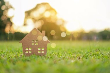 Güneş ışığı arka plan ile yeşil çim üzerinde küçük ev modeli kapalı.