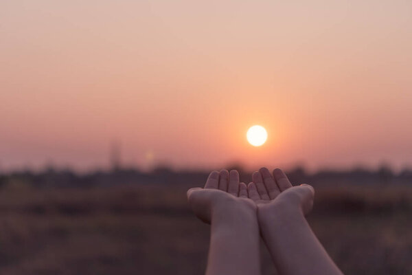 Woman hands place together like praying in front of nature blur beach sunset sky background.