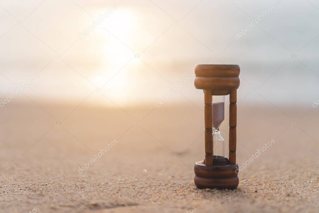 Small hourglass show time is flowing on sand beach texture background.