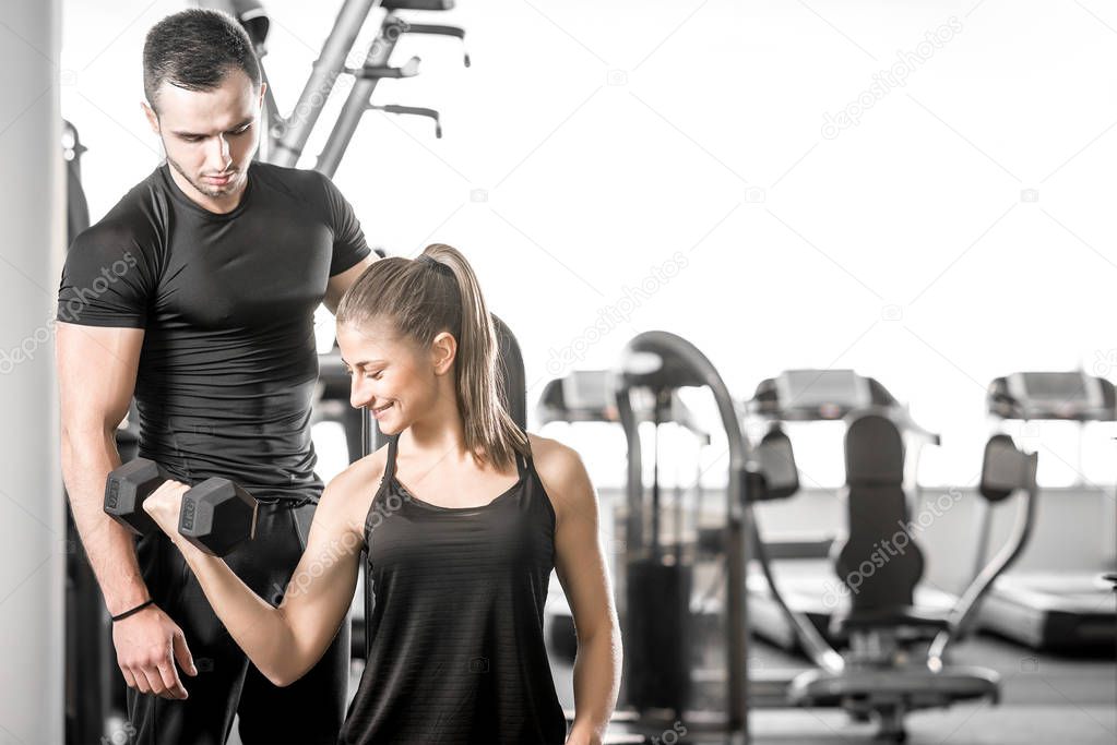 Woman doing bicep curls in gym with her personal trainer
