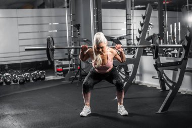 Modern spor salonunda çömelme hareketleri yapan bir sarışın..