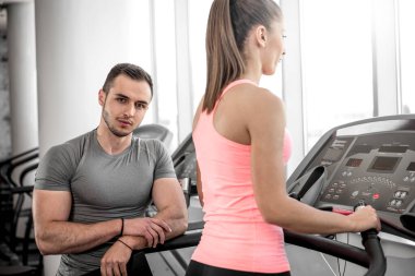 Modern bir fitness studio tesiste koşu bandı üzerinde yürürken özel müvekkilinin izlerken kişisel fitness eğitmeni.